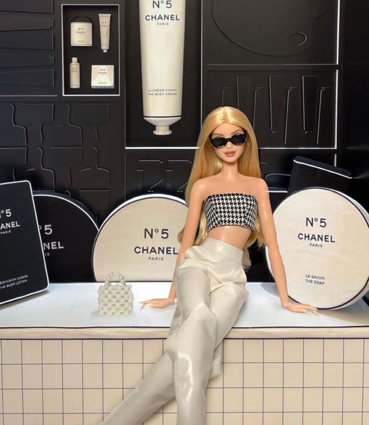 a barbie doll sitting on top of a counter in front of chanel bottles and sunglasses