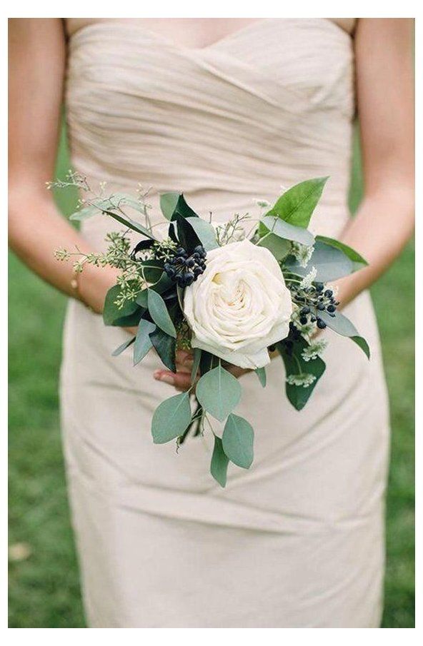 a woman in a dress holding a white flower bouquet with green leaves and greenery