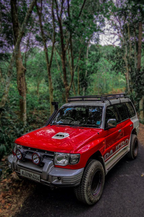 a red car parked on the side of a dirt road in front of some trees