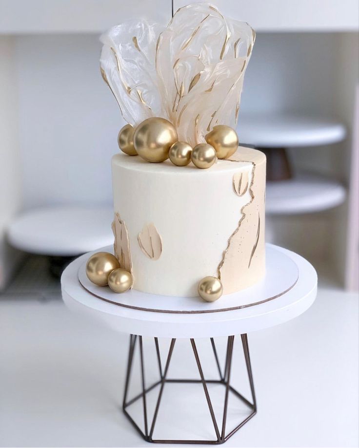 a white and gold cake on a stand with some golden balls around it's edges