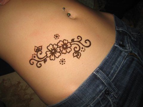 a woman's back tattoo with flowers and leaves on her left side ribcage