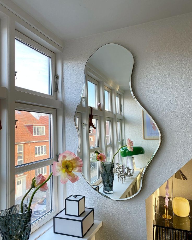 a mirror hanging on the side of a wall next to a vase with flowers in it