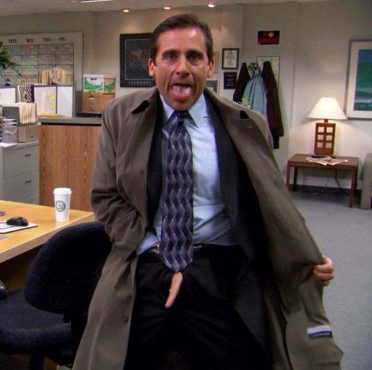 a man in a trench coat and tie sitting at a desk with his mouth open