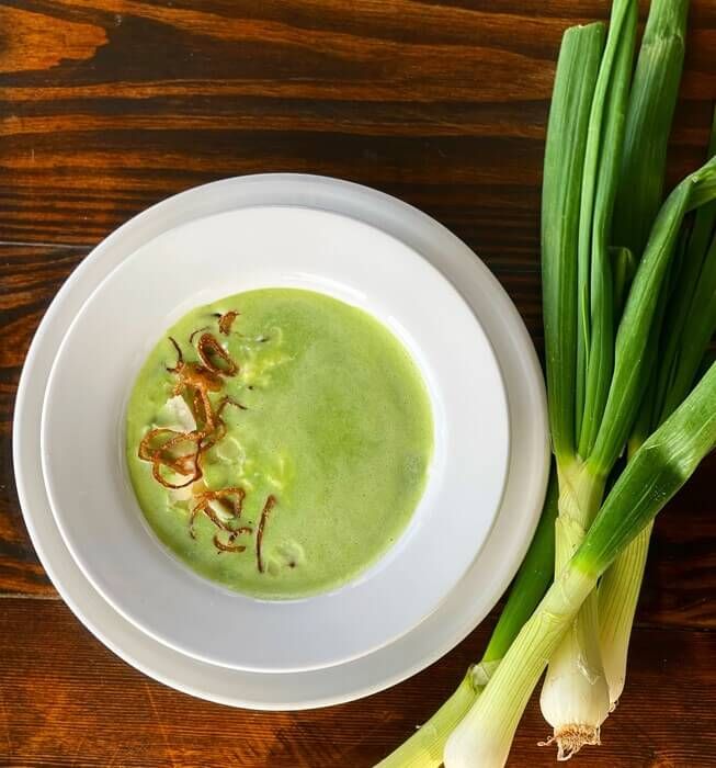 there is a bowl of soup on the table next to some green onions and celery