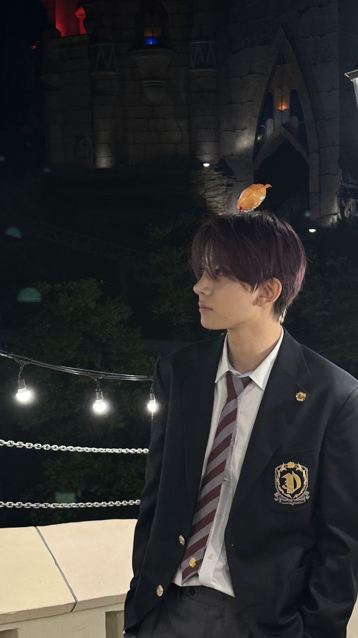 a young man in a suit and tie sitting on a ledge with lights behind him