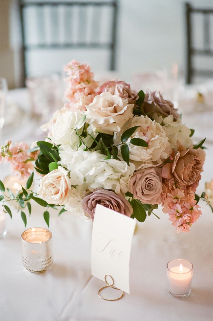 a bouquet of flowers sitting on top of a table next to two votive candles