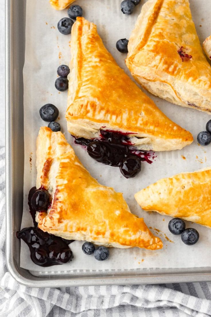 blueberry turnovers on a baking sheet with fresh berries and syrup in the background