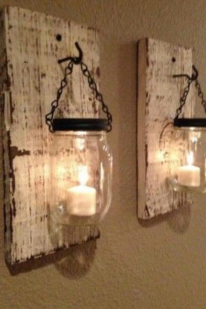 two mason jars are hanging on the wall with candles in them and one is holding a lit candle