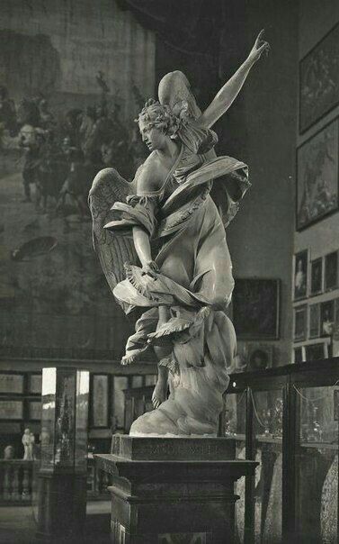 an antique photo of a statue in the middle of a room with pictures on the walls