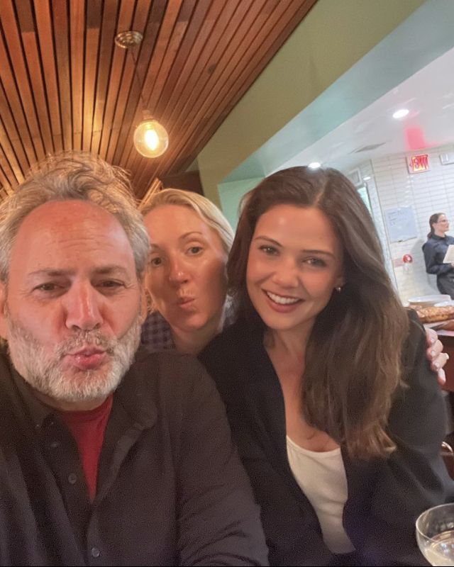 three people sitting at a table with wine glasses in front of them and one person making a funny face