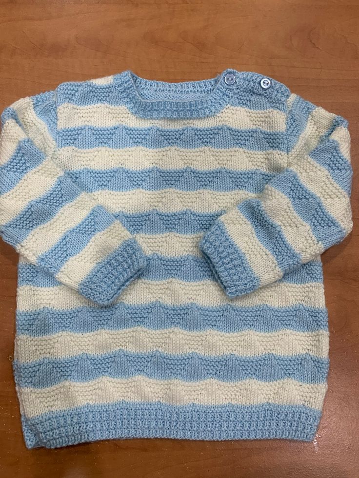 a blue and white striped sweater sitting on top of a wooden table next to a pair of scissors