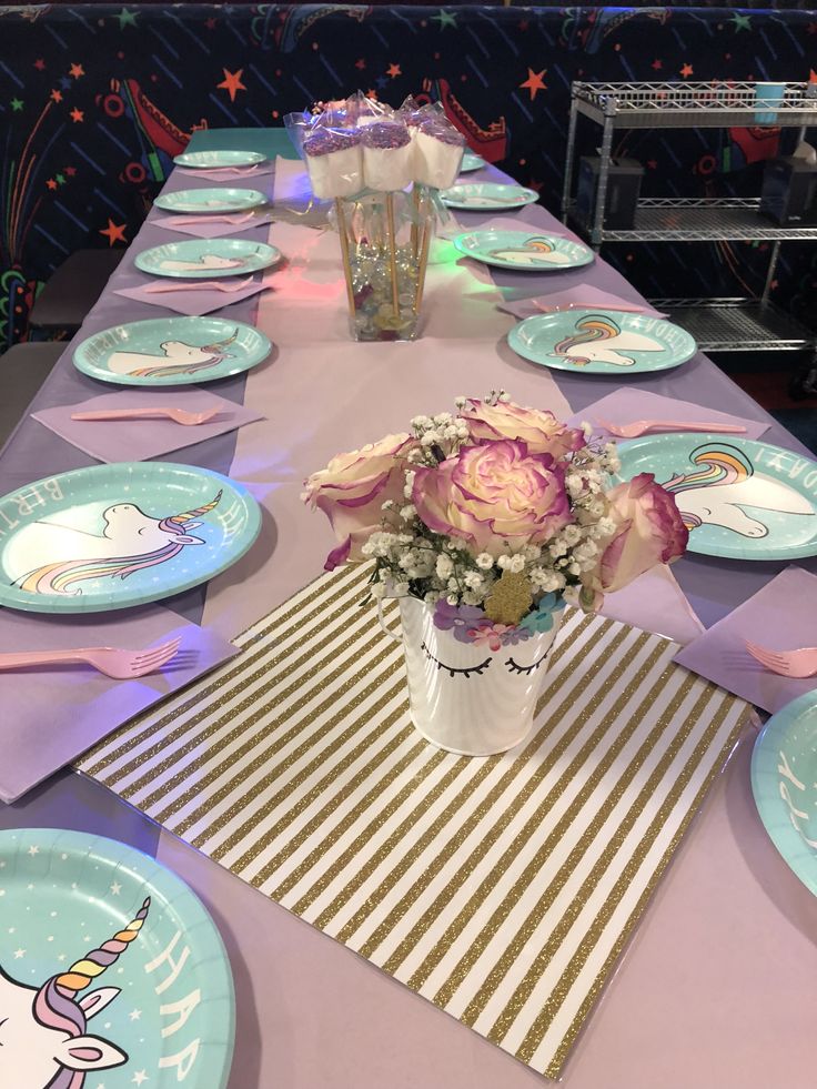 the table is set with plates, flowers and napkins for unicorn themed birthday party