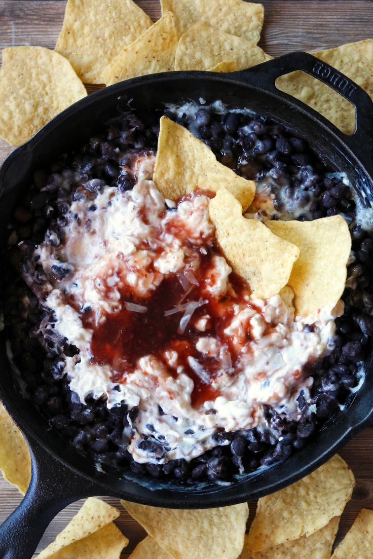 a skillet filled with black beans, tortilla chips and salsa dip surrounded by tortilla chips