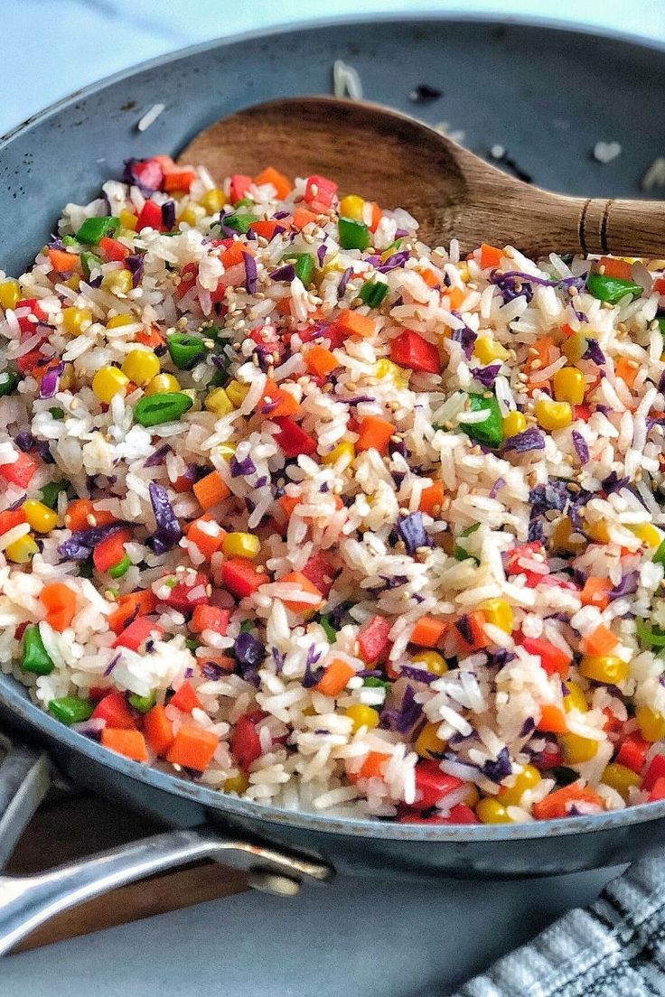 a pan filled with rice and vegetables on top of a table next to utensils