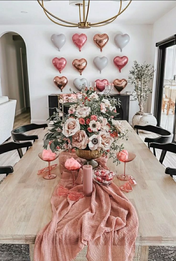 a dining room table decorated with pink and white flowers, heart shaped balloons on the wall