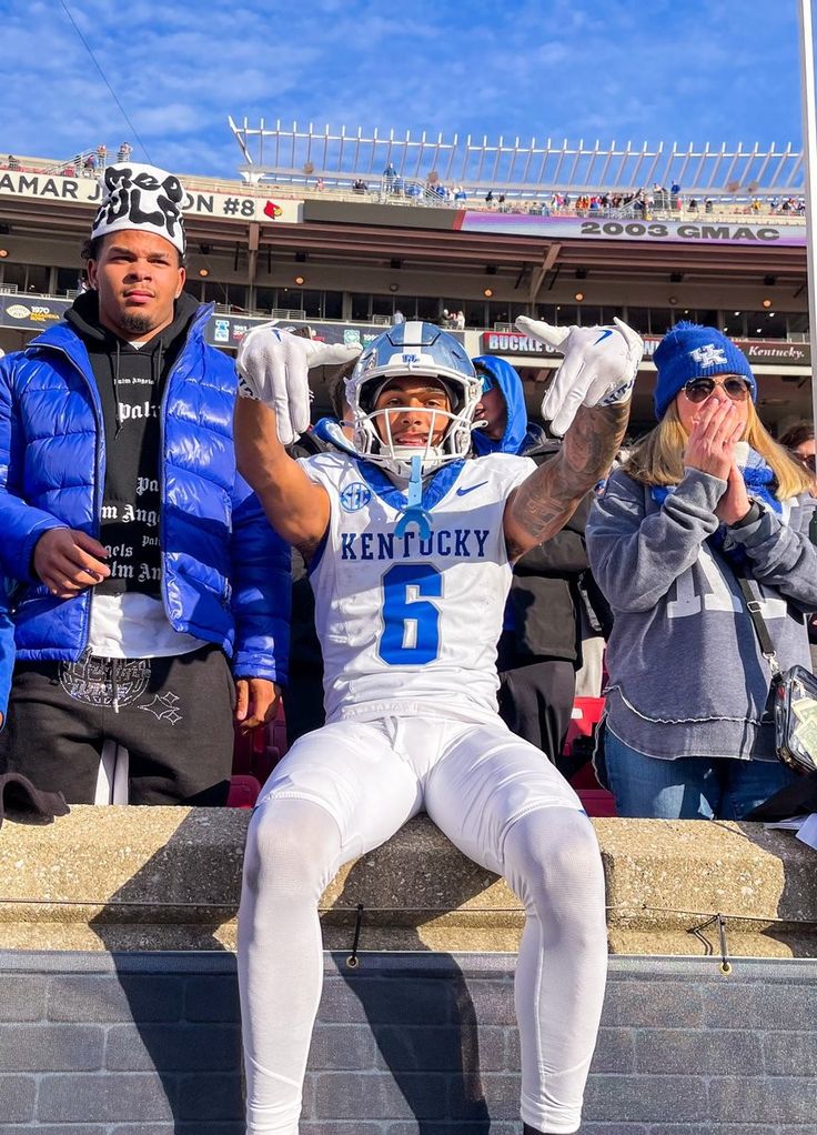 a football player sitting on the sidelines with his hands in the air and people standing behind him