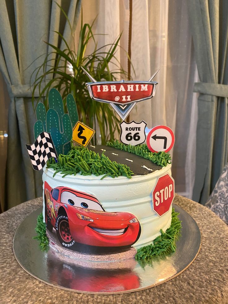 a birthday cake with cars on it sitting on a table next to a potted plant