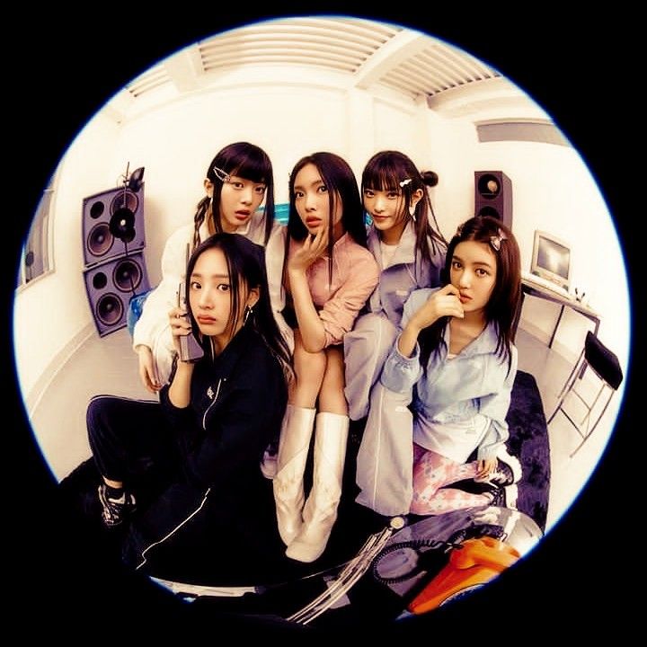 a group of young women sitting next to each other on top of a bed in front of speakers