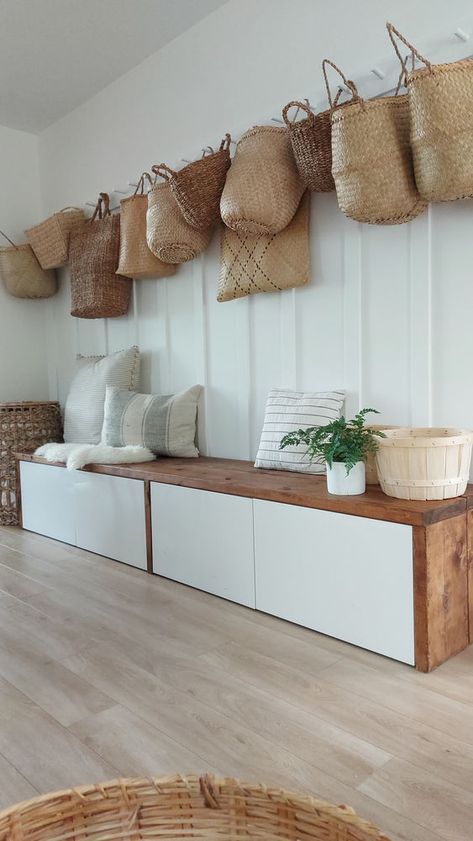 baskets hanging on the wall above a wooden bench with white drawers and storage units below