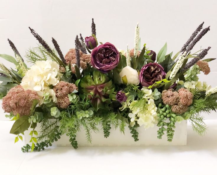 a white vase filled with lots of flowers and greenery