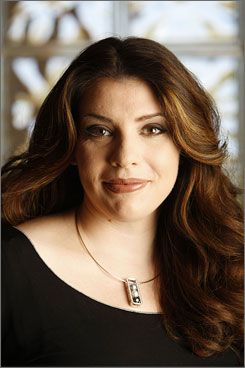 a woman with long brown hair wearing a black shirt and necklace smiling at the camera