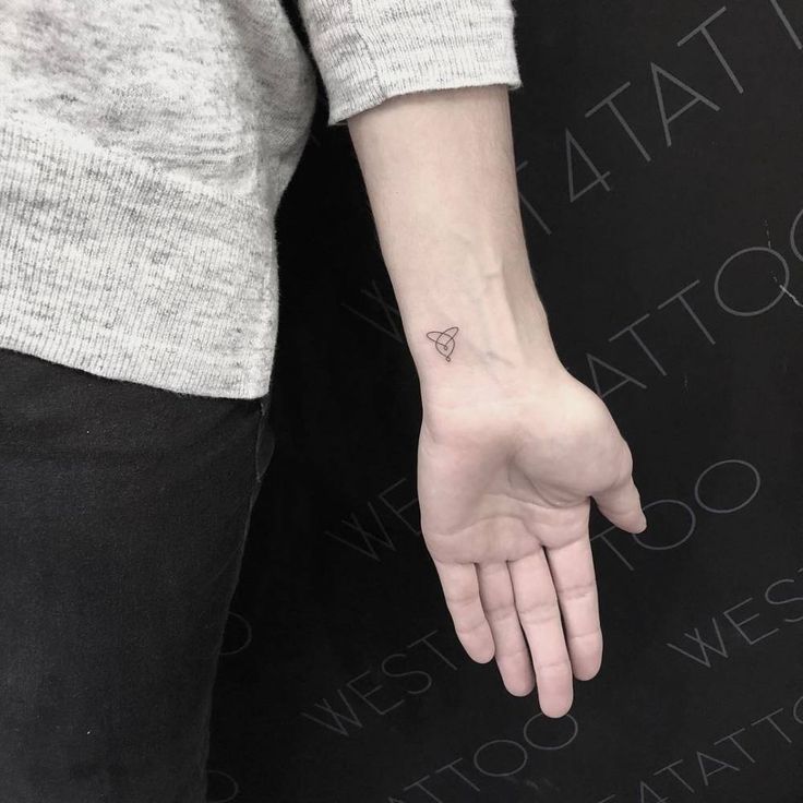 a woman's hand with a small triangle tattoo on her left wrist and the word tattoos written below it