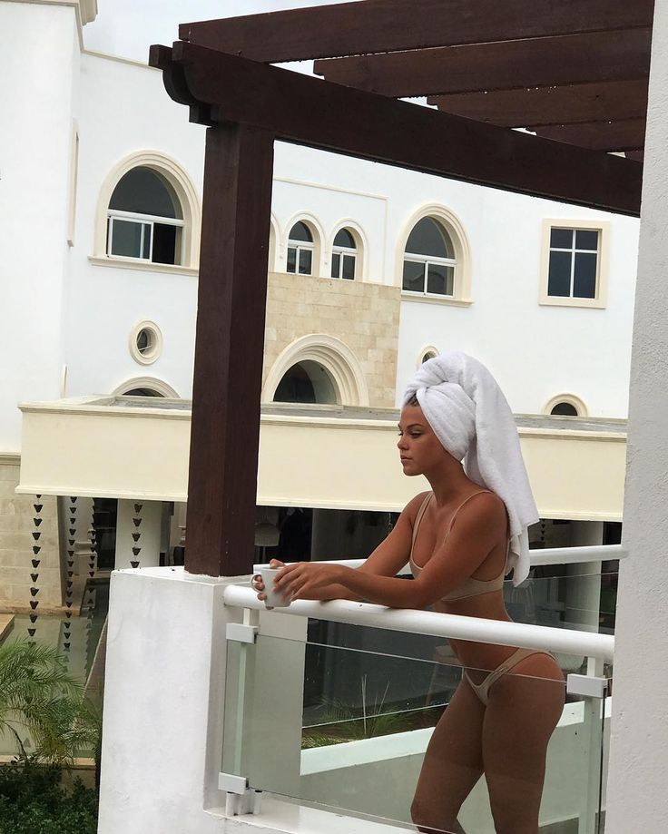 a woman with a towel on her head is standing on a balcony looking at the camera