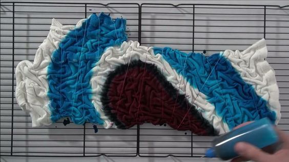 a person is using a blue and white brush to decorate a piece of cake on a wire rack