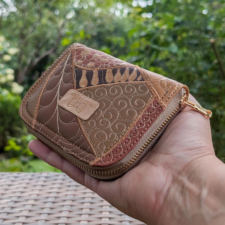 a hand holding a brown wallet on top of a wicker table next to trees