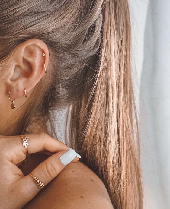 a close up of a person wearing gold rings and ear piercings on their ears