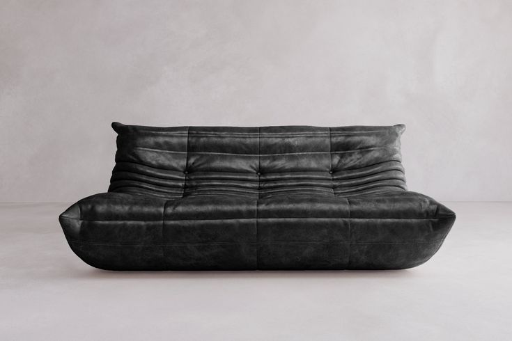 a black leather couch sitting on top of a white floor next to a gray wall