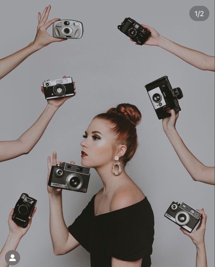 a woman in black dress surrounded by camera's and hand held up to her face