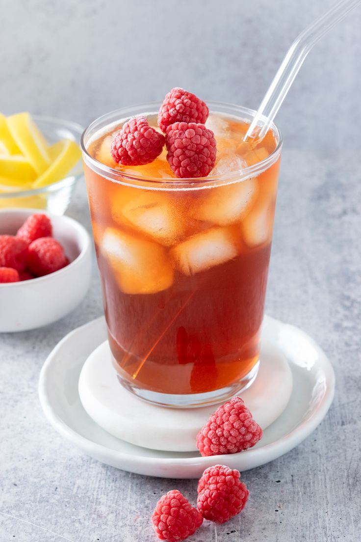 a glass filled with ice and raspberries on top of a white saucer