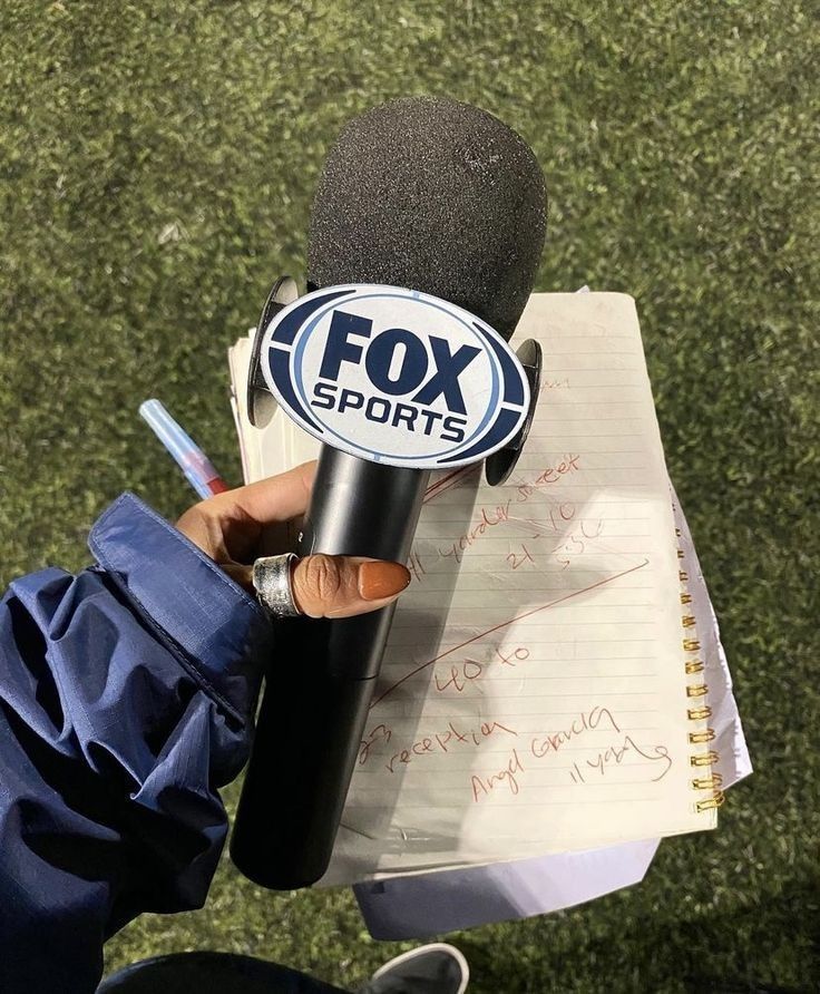 a person holding a microphone in front of a paper with the fox sports logo on it