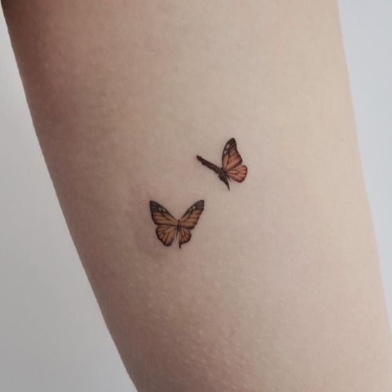 two small butterflies on the side of a woman's thigh, one is orange and the other is brown