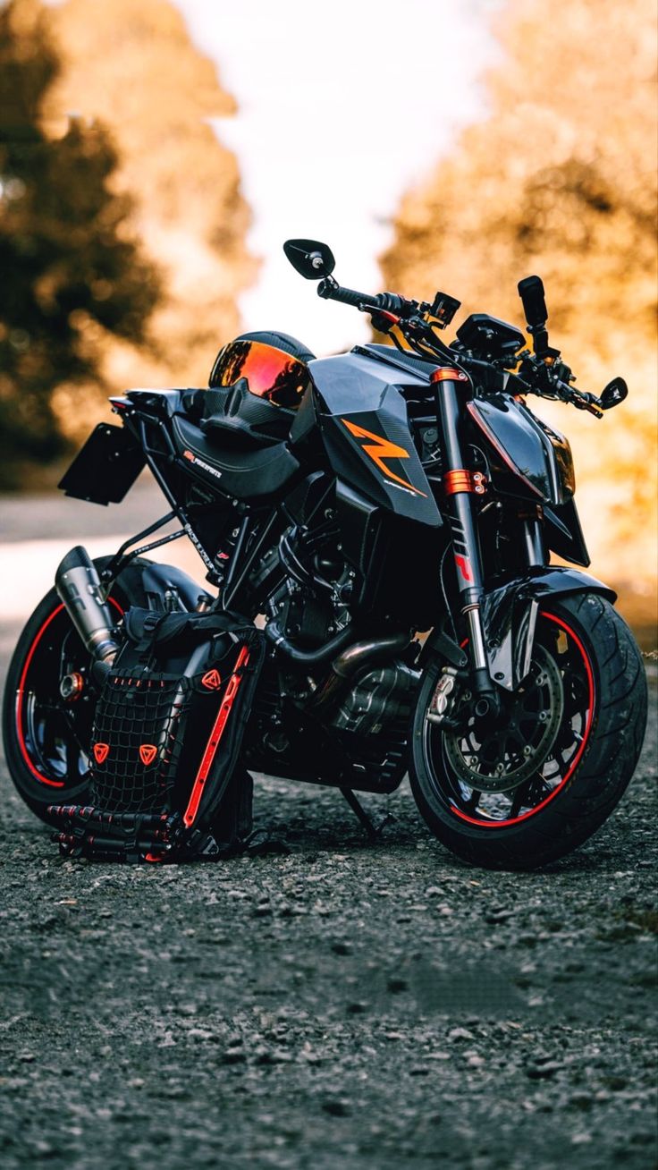 a black motorcycle parked on top of a gravel road next to trees in the background