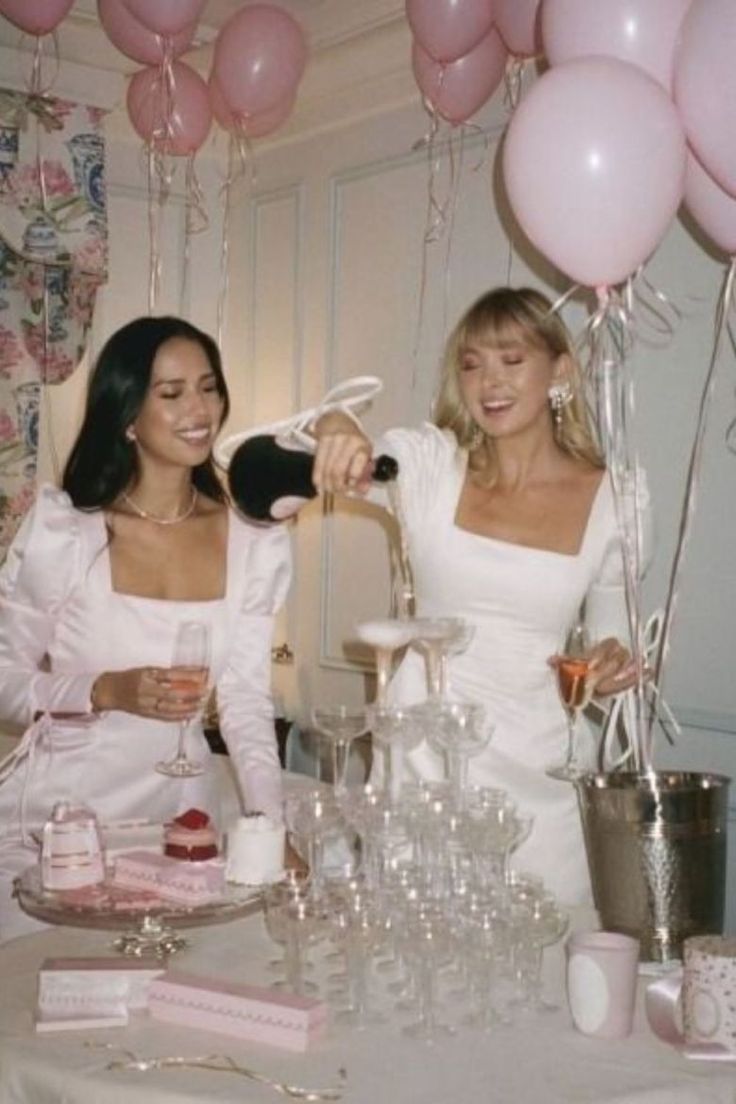 two beautiful women standing next to each other at a table with balloons and confetti