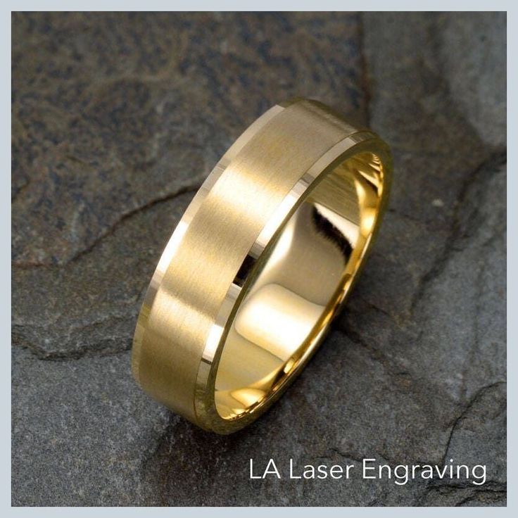 a yellow gold wedding ring on top of a stone slab with the words la laser engraving