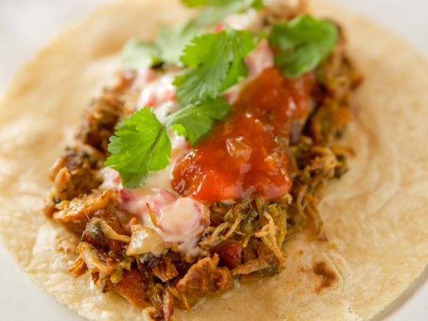 a tortilla topped with shredded meat, sauce and cilantro on a white plate