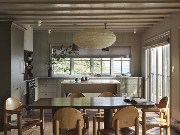 a dining room table and chairs in front of an open kitchen area with lots of windows