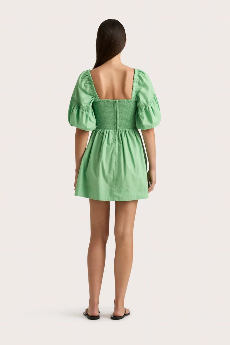 A 100% organic cotton mini dress in Apple with a fitted bodice and slightly-flared A-line skirt, gathered at the waist. A beloved FAITHFULL silhouette, it features further gathering on the front bodice and shirring at the back for additional stretch and movement. With a square neckline and elbow-length puff sleeves, elasticated at the cuff, style with a simple sandal for pop of colour in your everyday. Ruched Mini Dress With Fitted Waist, Spring Ruched Cotton Puff Sleeve Dress, Spring Ruched Puff Sleeve Cotton Dress, Spring Cotton Puff Sleeve Ruched Dress, Spring Cotton Puff Sleeve Dress With Ruched Details, Cotton Fit And Flare Mini Dress, Cotton Fit And Flare Mini Dress Knee-length, Cotton Fit And Flare Knee-length Mini Dress, Cotton Puff Sleeve Mini Dress With Smocked Back