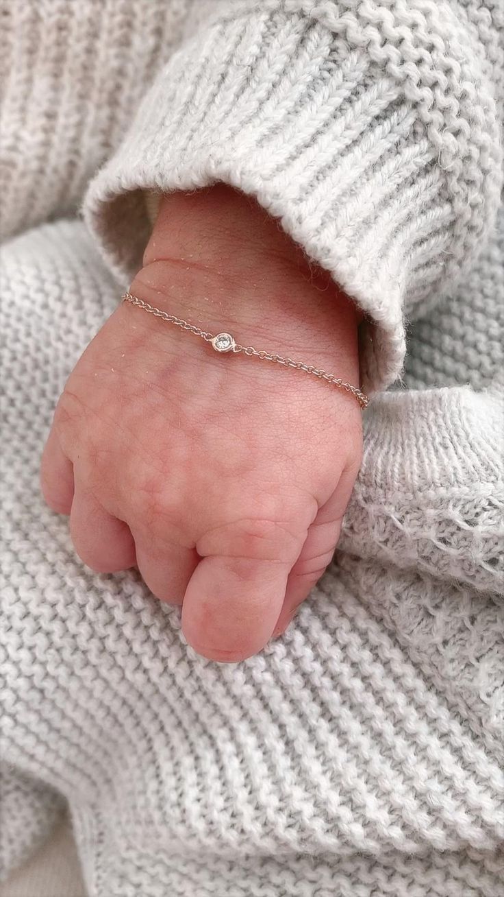 a baby's hand with a tiny white diamond on it, wrapped in a sweater