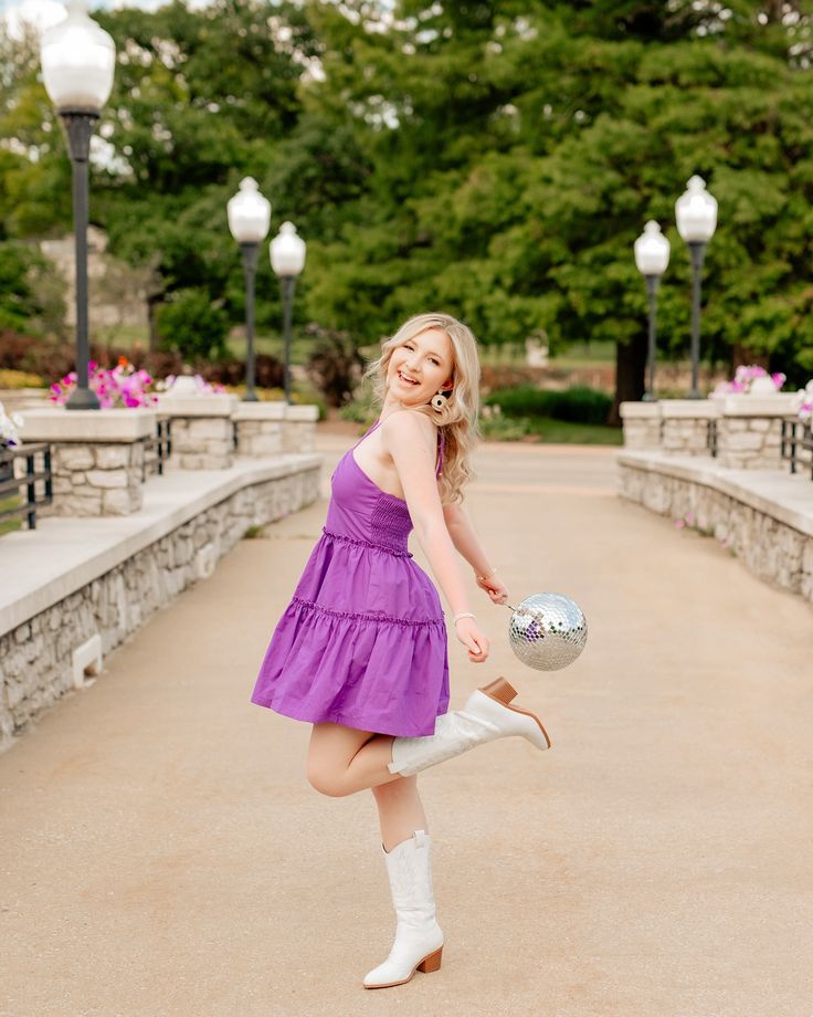 a woman in a purple dress is holding a silver ball and posing for the camera