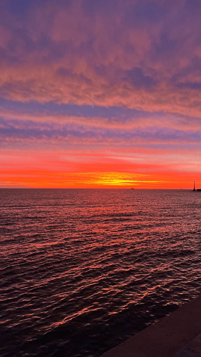 the sun is setting over the ocean with a boat in the distance