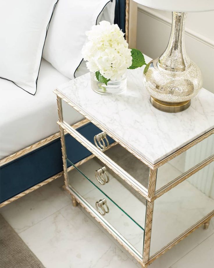 a white flower sitting on top of a mirrored table next to a bed and nightstand