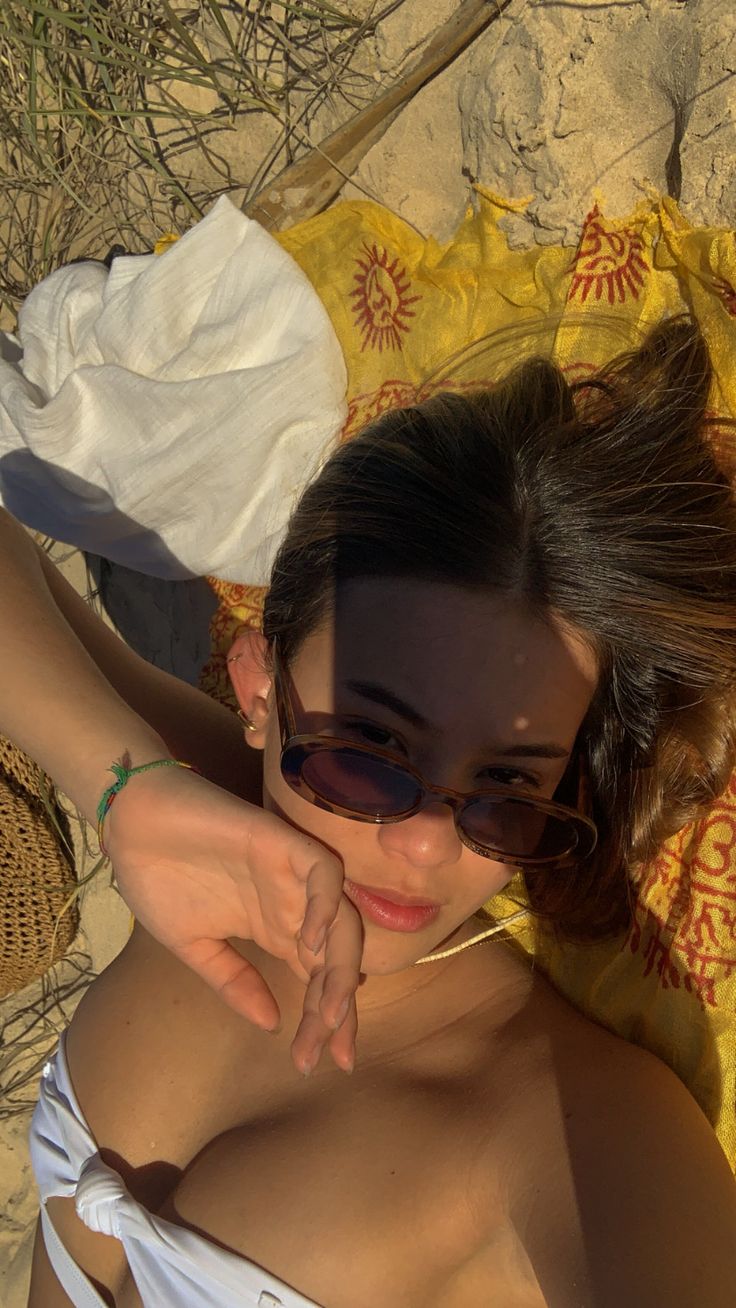 a woman laying on top of a beach next to a yellow towel and wearing sunglasses