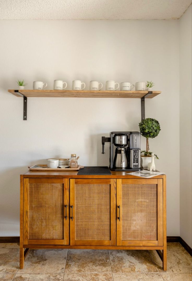 a wooden cabinet with some cups on top of it and a coffee maker in the corner