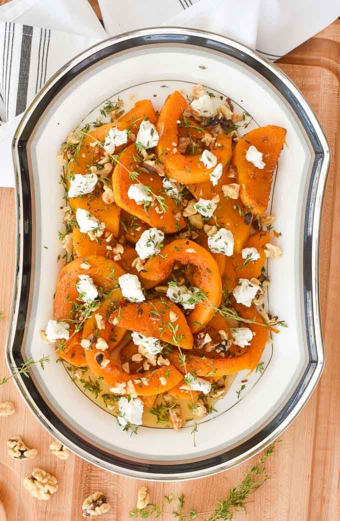 a white plate topped with carrots covered in feta cheese and herbs next to silverware