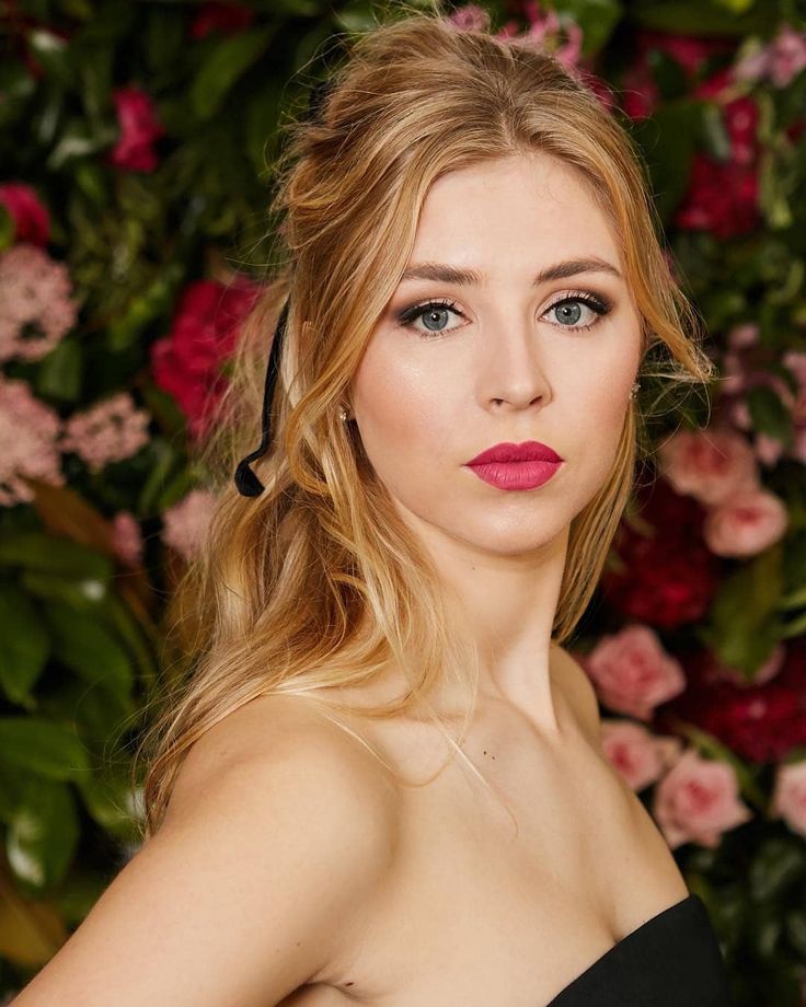 a woman with blonde hair and blue eyes wearing a black dress in front of flowers