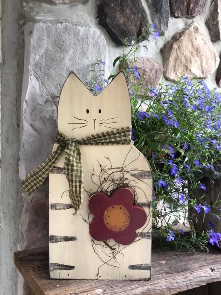 a wooden cat sitting on top of a table next to blue flowers and a stone wall